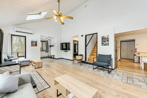 A spacious living area with a wooden floor, a ceiling fan, a flat-screen TV, and a staircase leading to another level. - Hot Tub & Game Room: Long Pond Getaway! (Long Pond)