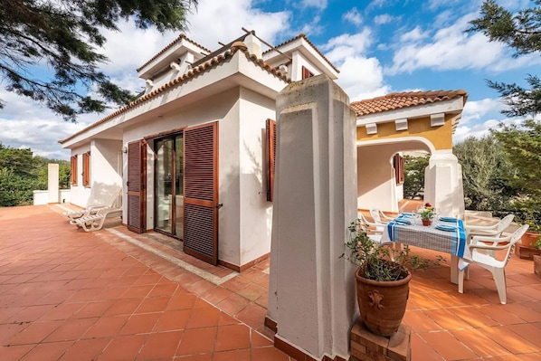 Una casa con patio de baldosas, una zona de estar techada al aire libre y una planta grande en maceta.
