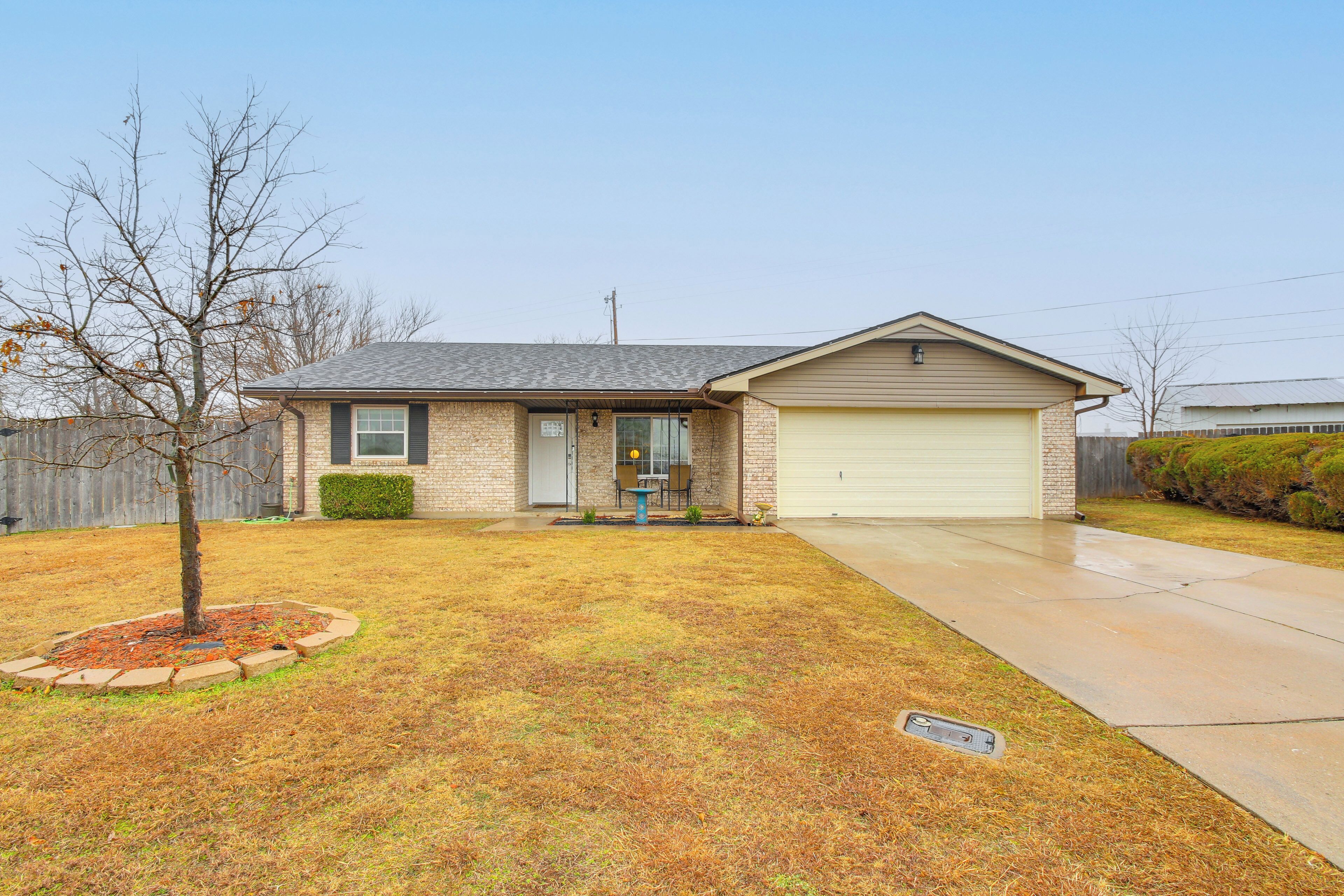 A single-story house with a garage, a front yard with a tree and a small garden bed, and a clear sky.
