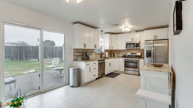 A modern kitchen with white cabinets, stainless steel appliances, and a sliding glass door leading to a patio with outdoor furniture. - 5 Mi to Museum of the Great Plains: Home w/ Patio (Lawton)
