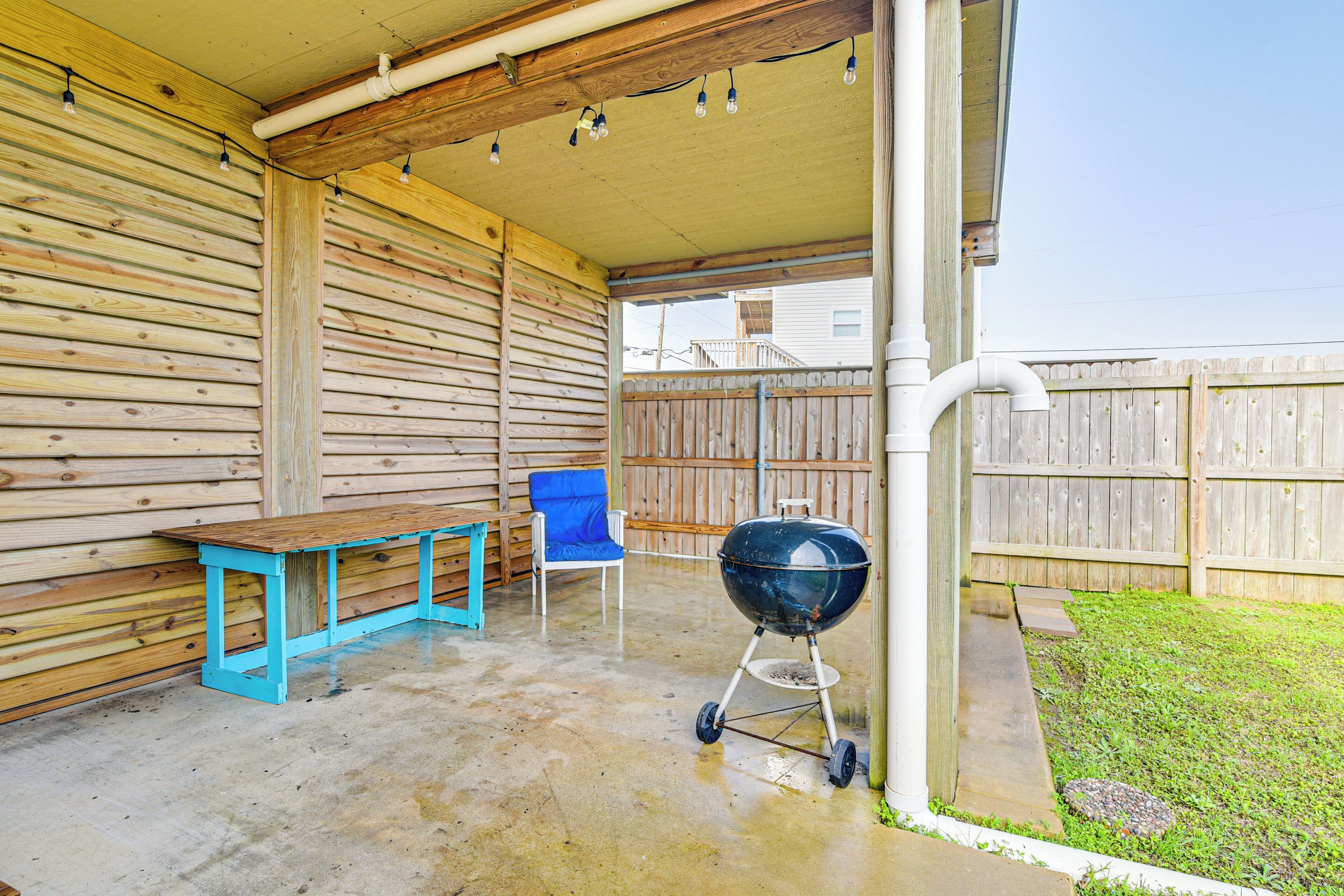 A covered patio with a wooden bench, a grill, and a chair.