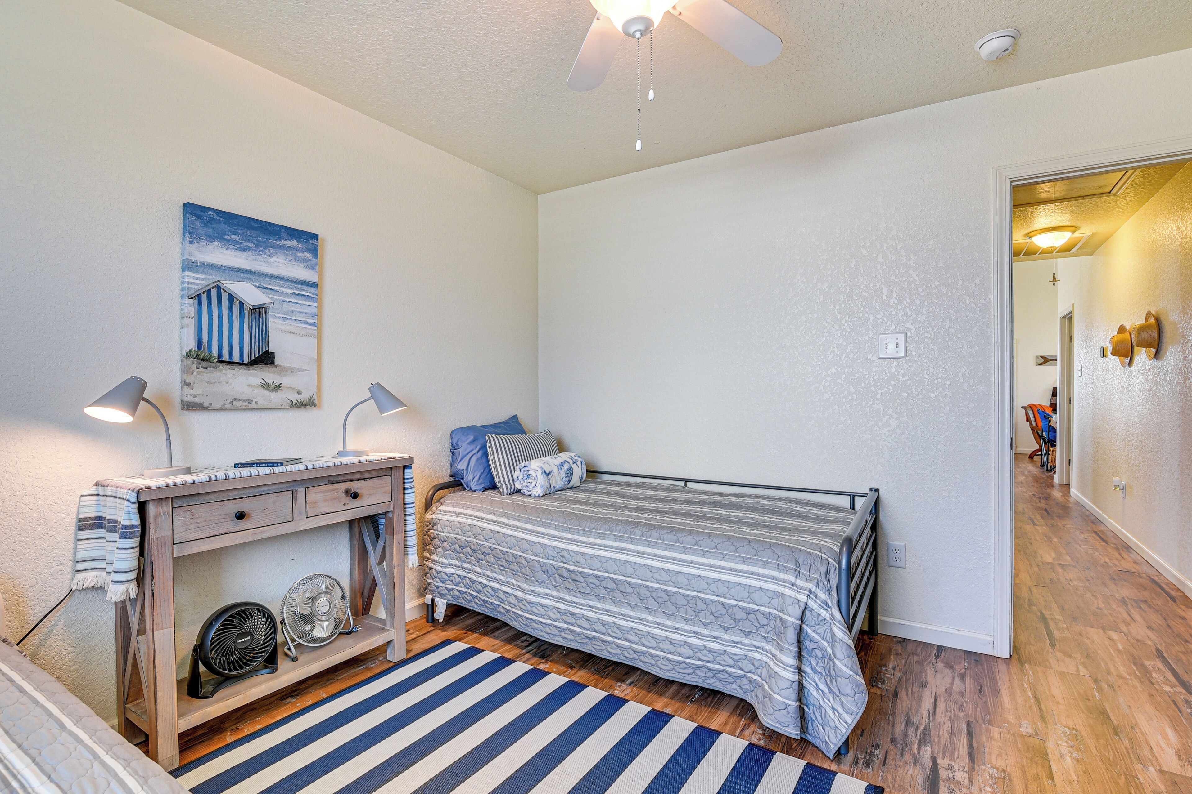 Um quarto com cama, escrivaninha com ventilador, quadro e ventilador de teto.