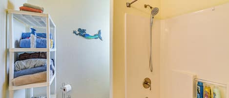 A bathroom with a shower, a shelf with towels, and toiletries.