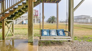 A wooden swing set with blue cushions, a wooden staircase, and a view of a beach and buildings in the background. - Walk to Beach; Surfside Beach Home w/ Deck (Freeport)
