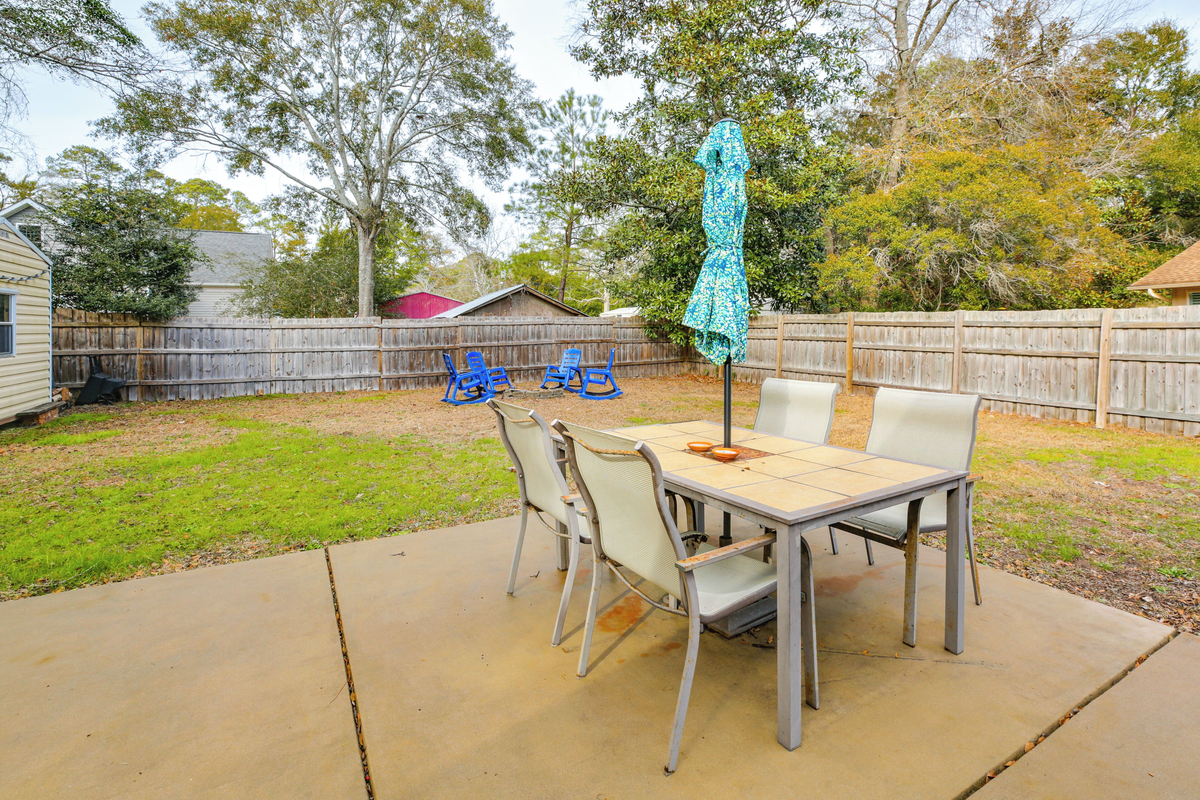 A patio with a table and chairs, a covered umbrella, and a wooden fence in the background.