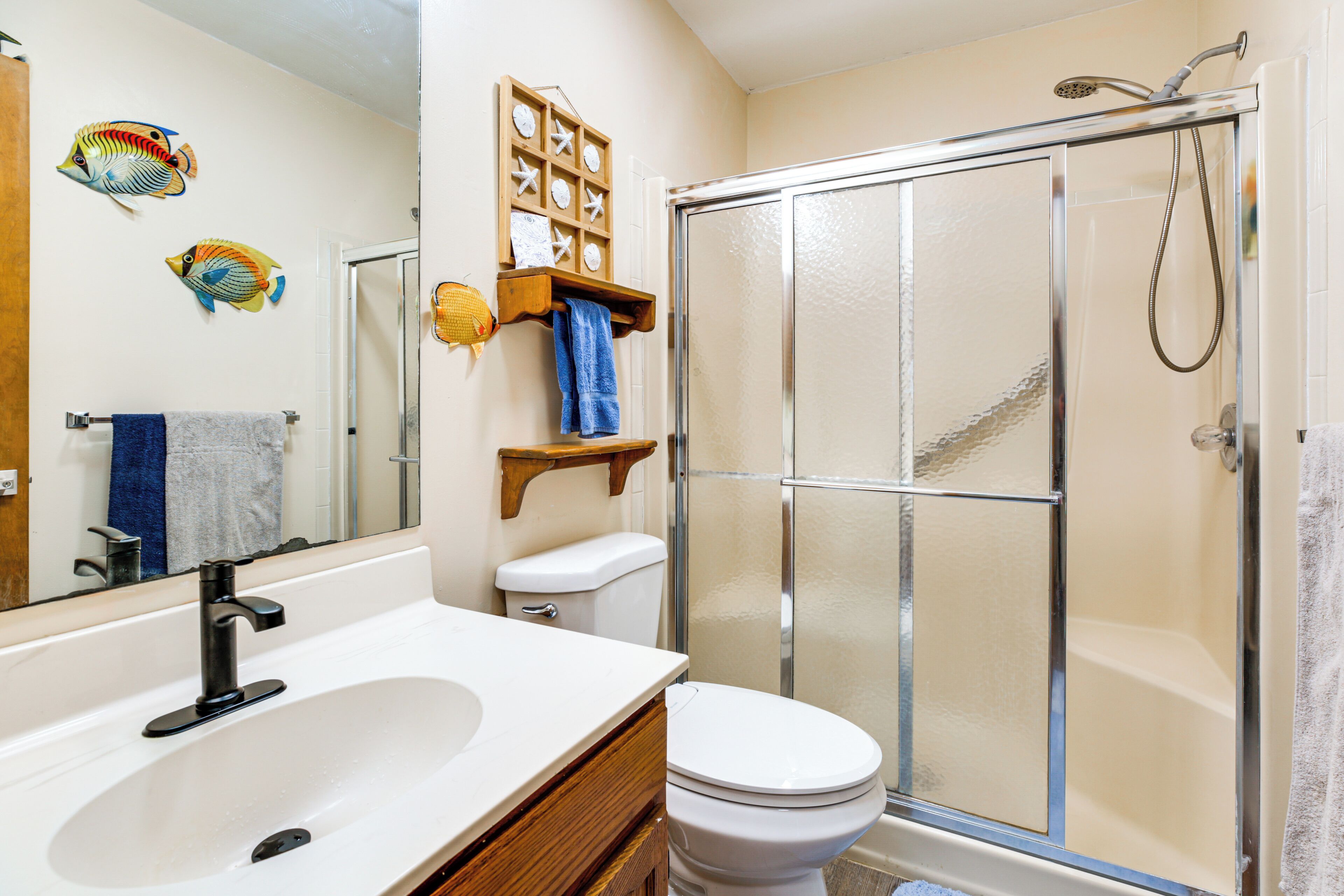 A bathroom with a white sink, a toilet, a shower enclosure, and decorative fish wall art.