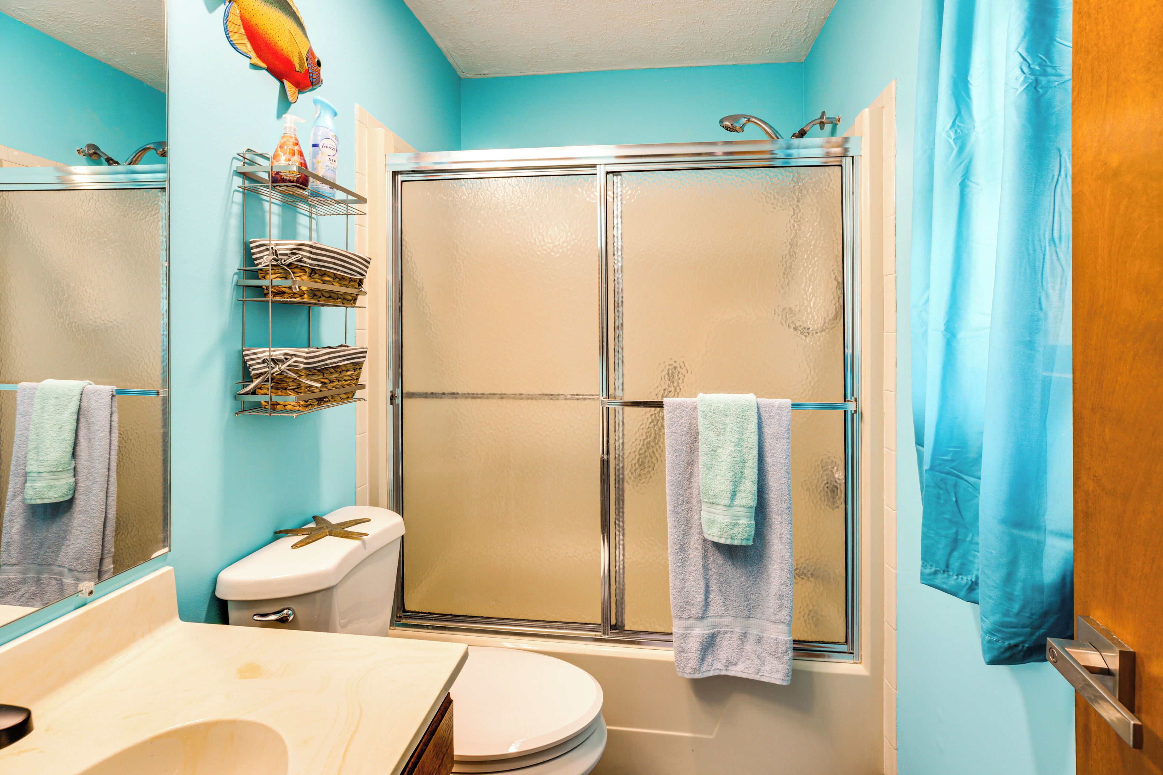 A bathroom with a glass-enclosed shower, a toilet, a sink, and a shelf with toiletries.
