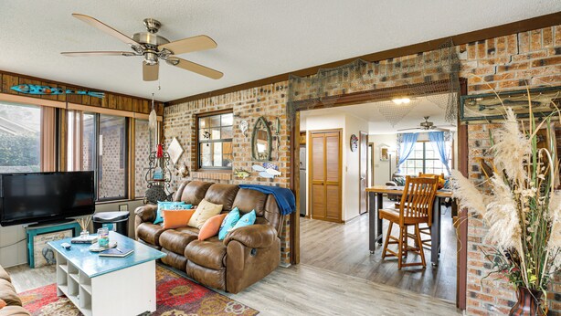 A spacious living room with a leather sofa, a television, and a dining area with a wooden table and chairs. - Cozy Home w/ Fenced Backyard in Sunset Beach! (Sunset Beach)