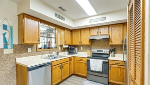 A kitchen with wooden cabinets, a dishwasher, a stove, and a coffee maker. - Cozy Home w/ Fenced Backyard in Sunset Beach! (Sunset Beach)
