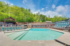 A swimming pool with lounge chairs and a covered seating area, surrounded by trees.