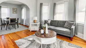 Un salon moderne avec un canapé gris, une table basse ronde et un coin repas comprenant une table et des chaises blanches.