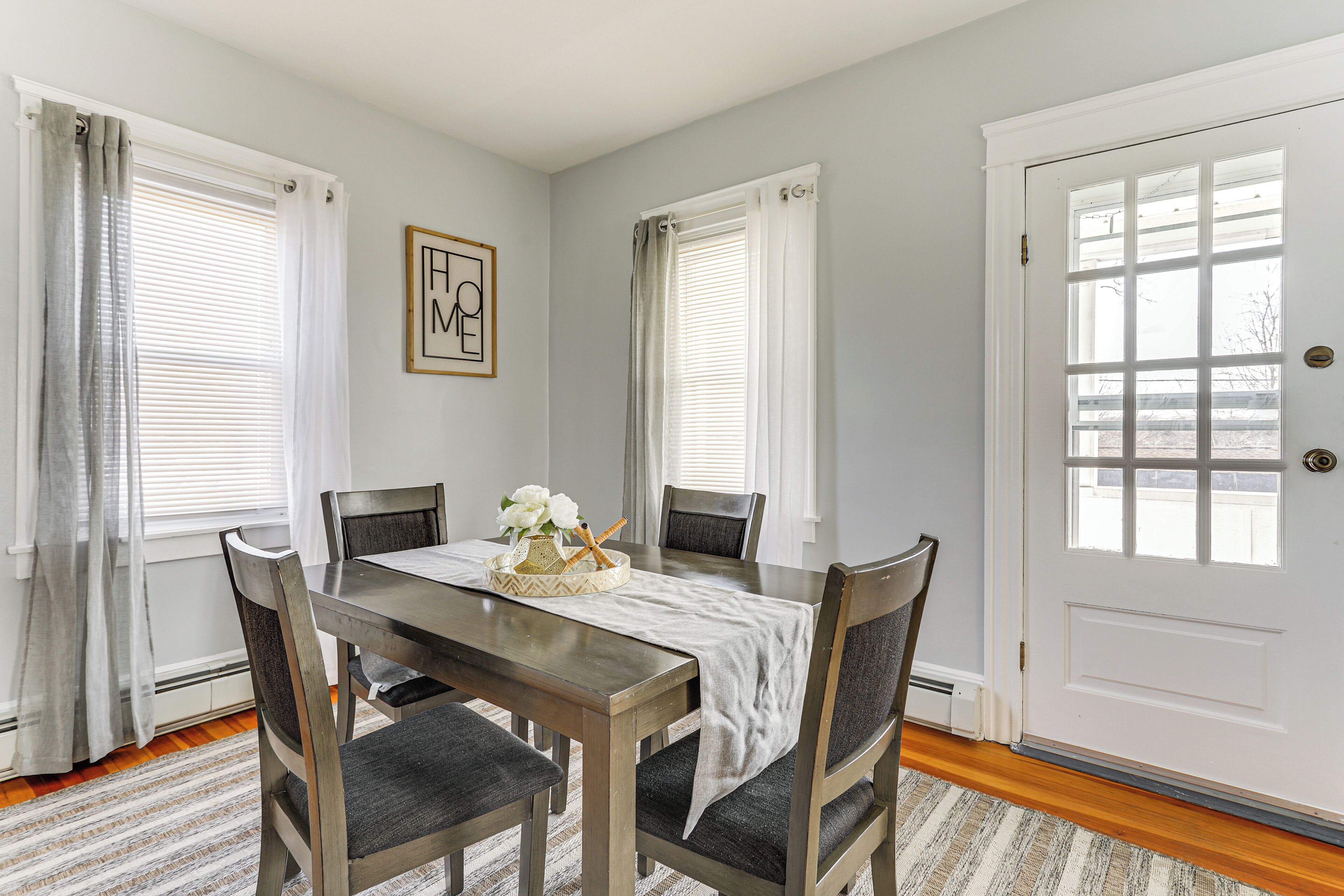 A dining room with a wooden table, four chairs, and a white door.