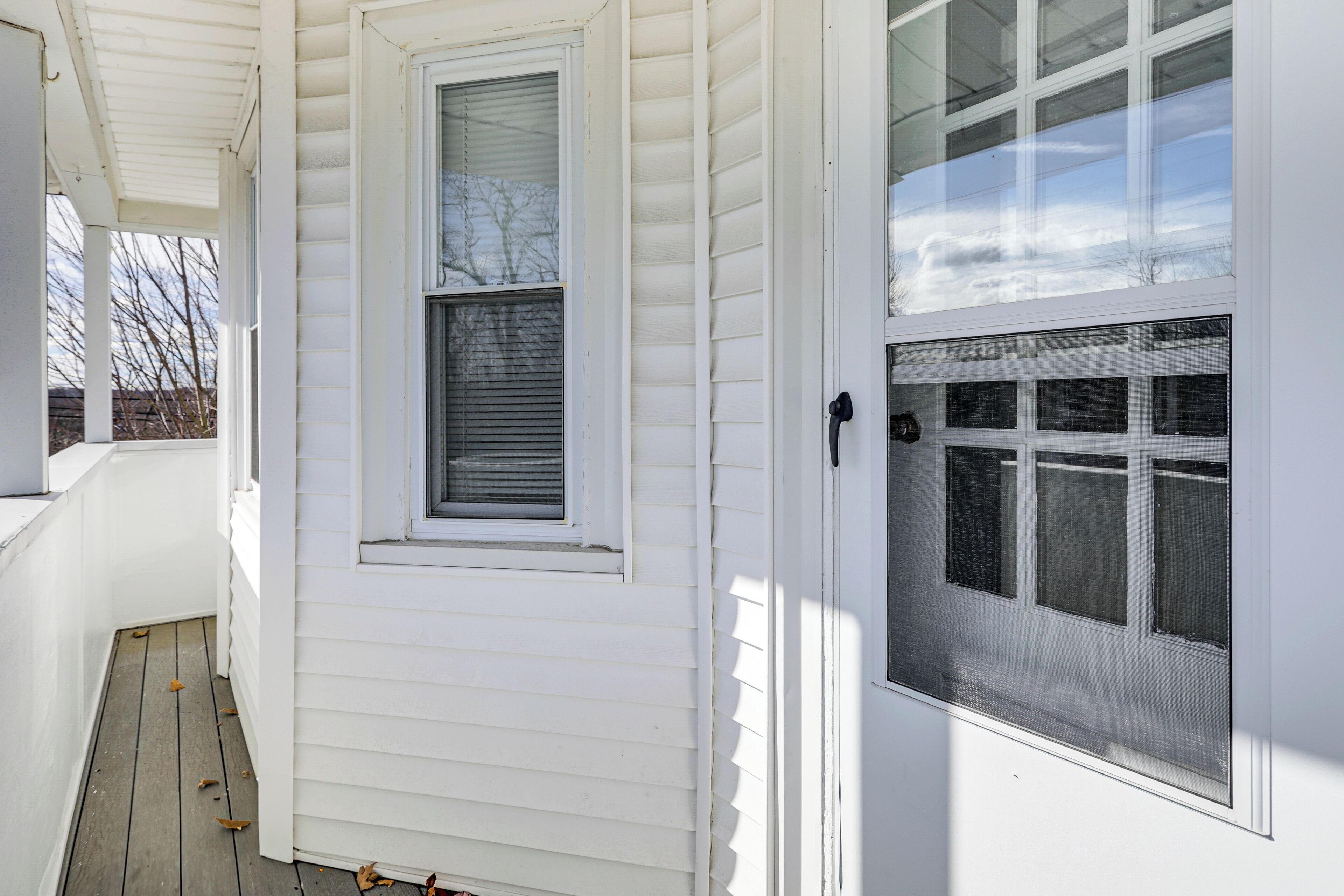 Fachada blanca de una casa con porche cubierto, ventana con persianas y puerta de garaje con varios ventanales.
