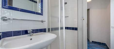 A bathroom with a white sink, a glass shower enclosure, and blue-tiled walls.