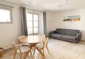Ein Wohnzimmer mit grauem Sofa, einem runden Holzes Esstisch mit Stühlen und einem Fenster mit Vorhängen.