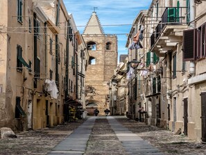 A narrow cobblestone street flanked by historic buildings with balconies and laundry hanging out to dry.
