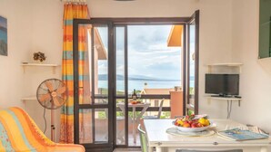 Ein Zimmer mit einer Couch, einem Tisch mit Früchten, einem Fernseher und einem Balkon mit Blick.