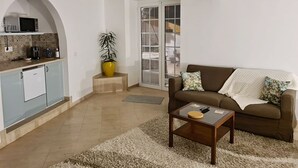 Een moderne woonkamer met een bank, salontafel en een keukenhoek met een magnetron en koffiezetapparaat.