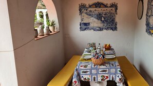 Een eethoek met een tafel voor twee, gedekt met een blauw-wit geruit tafelkleed, omringd door muren versierd met blauw-witte tegels waarop landelijke taferelen afgebeeld zijn.