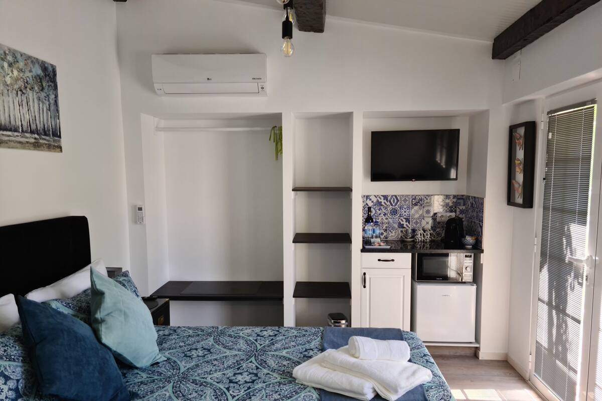 Une chambre à coucher comprenant un lit, une table de chevet et donnant sur un espace cuisine.