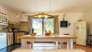 Une cuisine avec une table en bois, un banc, un réfrigérateur et une fenêtre avec des rideaux.