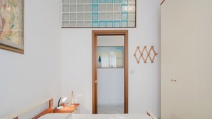 A hotel room with a bed, a nightstand, a lamp, a towel, a wardrobe, a mirror, and a decorative wall piece. - Breathtaking Seaview Flat in Sardinia (Porto Torres)