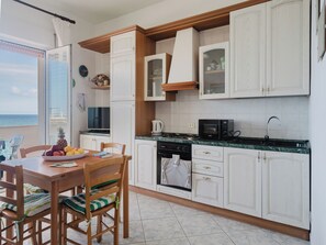 A kitchen with white cabinets, a dining table with chairs, a view of the ocean, and a small island with a kettle. - Breathtaking Seaview Flat in Sardinia (Porto Torres)
