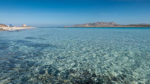 A clear coastal beach with rocky terrain and a distant mountain range. - Breathtaking Seaview Flat in Sardinia (Porto Torres)