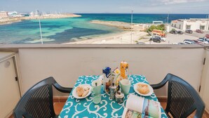 A balcony with a table set for breakfast, overlooking a beach and marina. - Breathtaking Seaview Flat in Sardinia (Porto Torres)