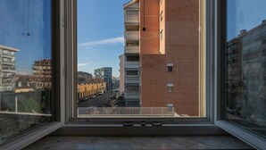 Vista desde una ventana que da a un paisaje urbano con una mezcla de edificios modernos y tradicionales, cielo despejado y una calle abajo.