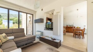 Una sala de estar moderna con un ventanal grande, un televisor de pantalla plana, un sofá y un comedor con muebles de madera.