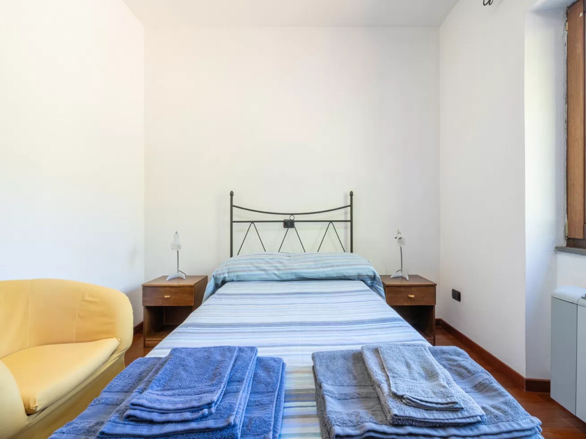 Un dormitorio con cama, dos mesitas de noche, una silla y una ventana.