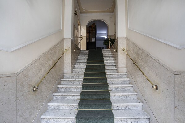 Una escalera de mármol con alfombra verde, bordeada por paredes y una puerta en la parte superior.