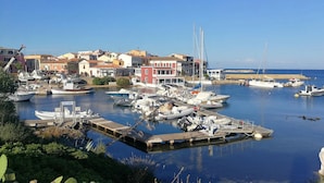 Un puerto deportivo con varias embarcaciones amarradas, un muelle de madera y edificios al fondo.