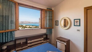 Un dormitorio con cama, mesita de noche, espejo y ventana con cortinas.