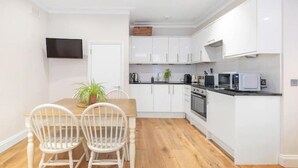 Een moderne keuken met witte kasten, een houten eettafel met twee stoelen en een flatscreen televisie aan de muur.