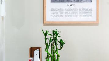 Fotografia em preto e branco emoldurada de um farol e edifícios em Maine, uma mesa de cabeceira de madeira com um controle remoto, uma planta de bambu e um livro.