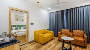 Una habitación de hotel con una cama, un sofá amarillo, dos sillones de cuero marrón, una mesita y una ventana con cortinas.