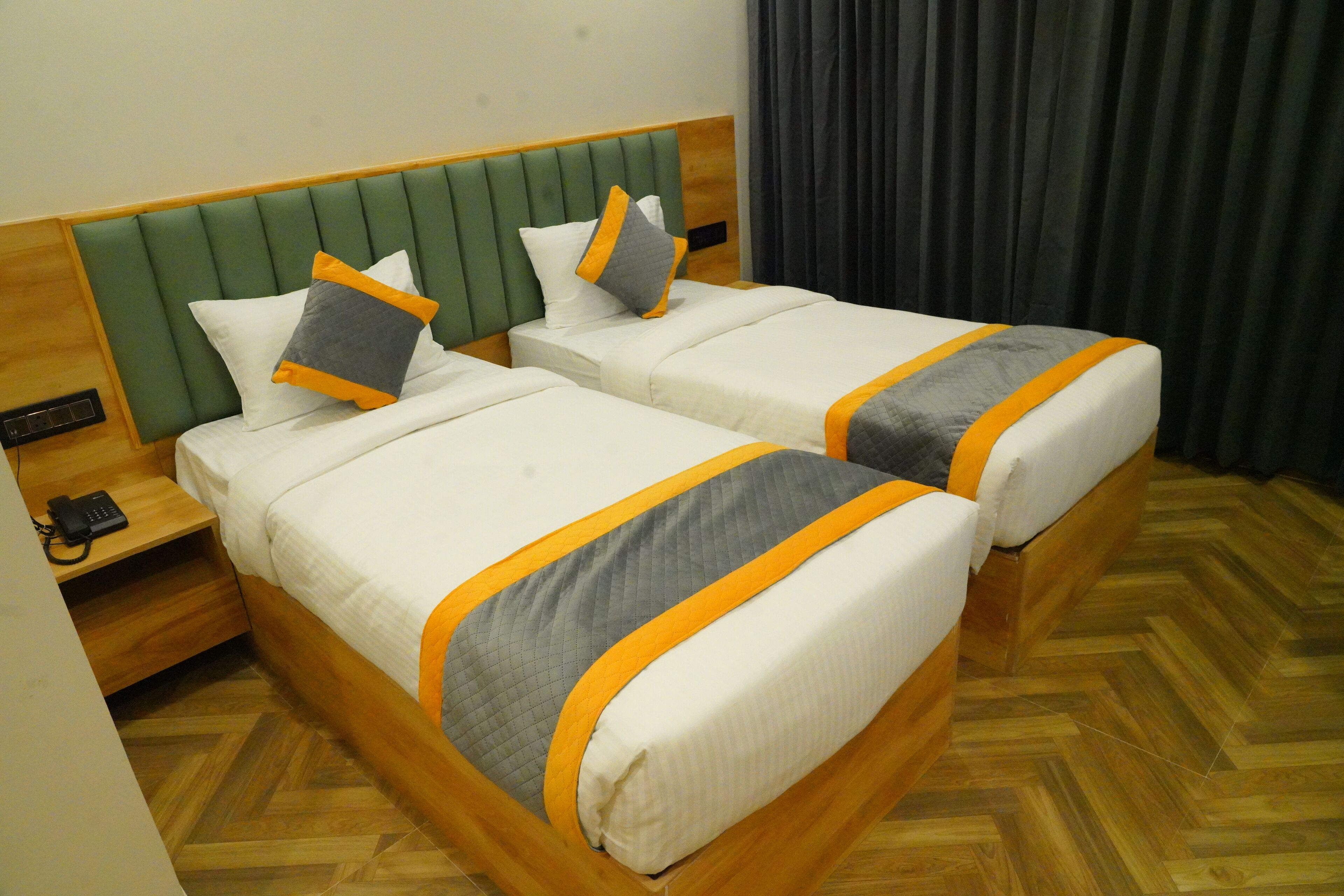 Duas camas com cabeceiras iguais, um criado-mudo de madeira com telefone, e um chão com padrão herringbone.