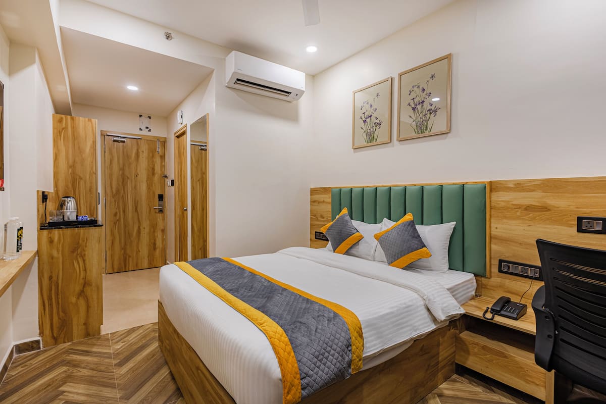 Habitación de hotel con cama de madera, escritorio con teléfono y cabecero tapizado en verde.