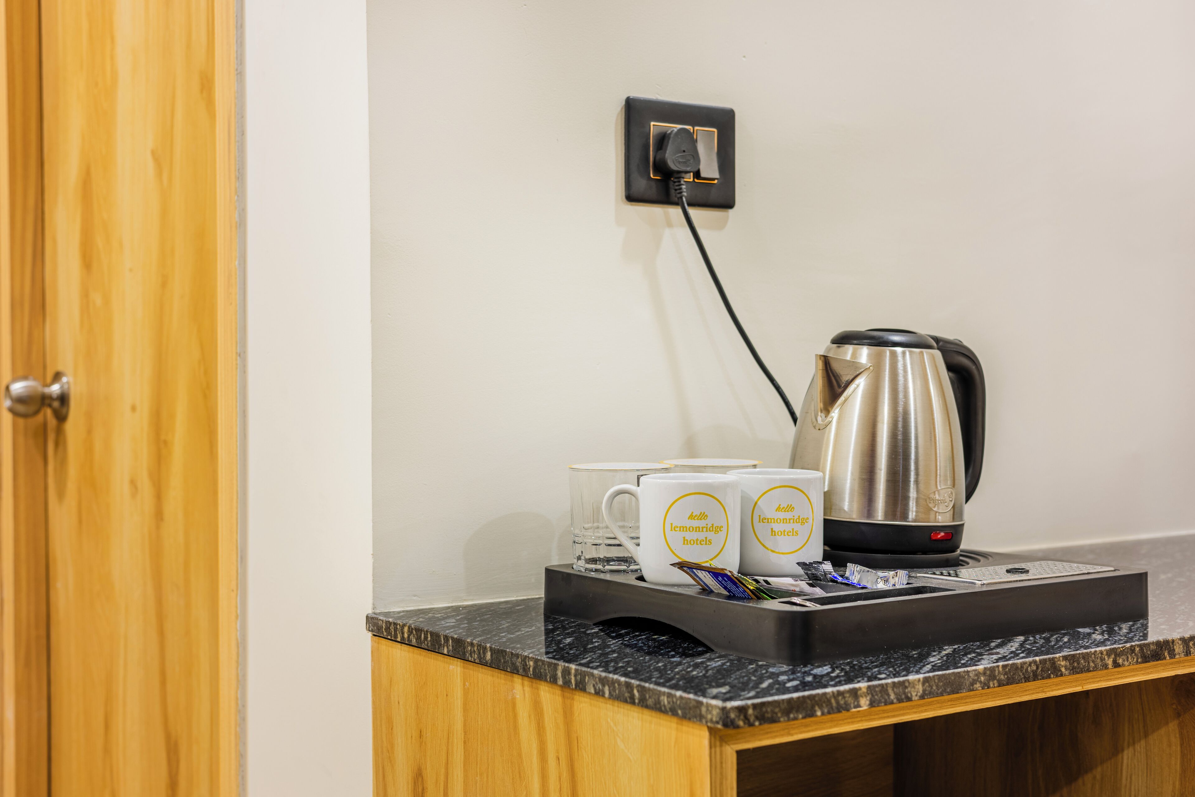 A countertop with a coffee maker, two mugs, and a tray with pens and a smartphone.