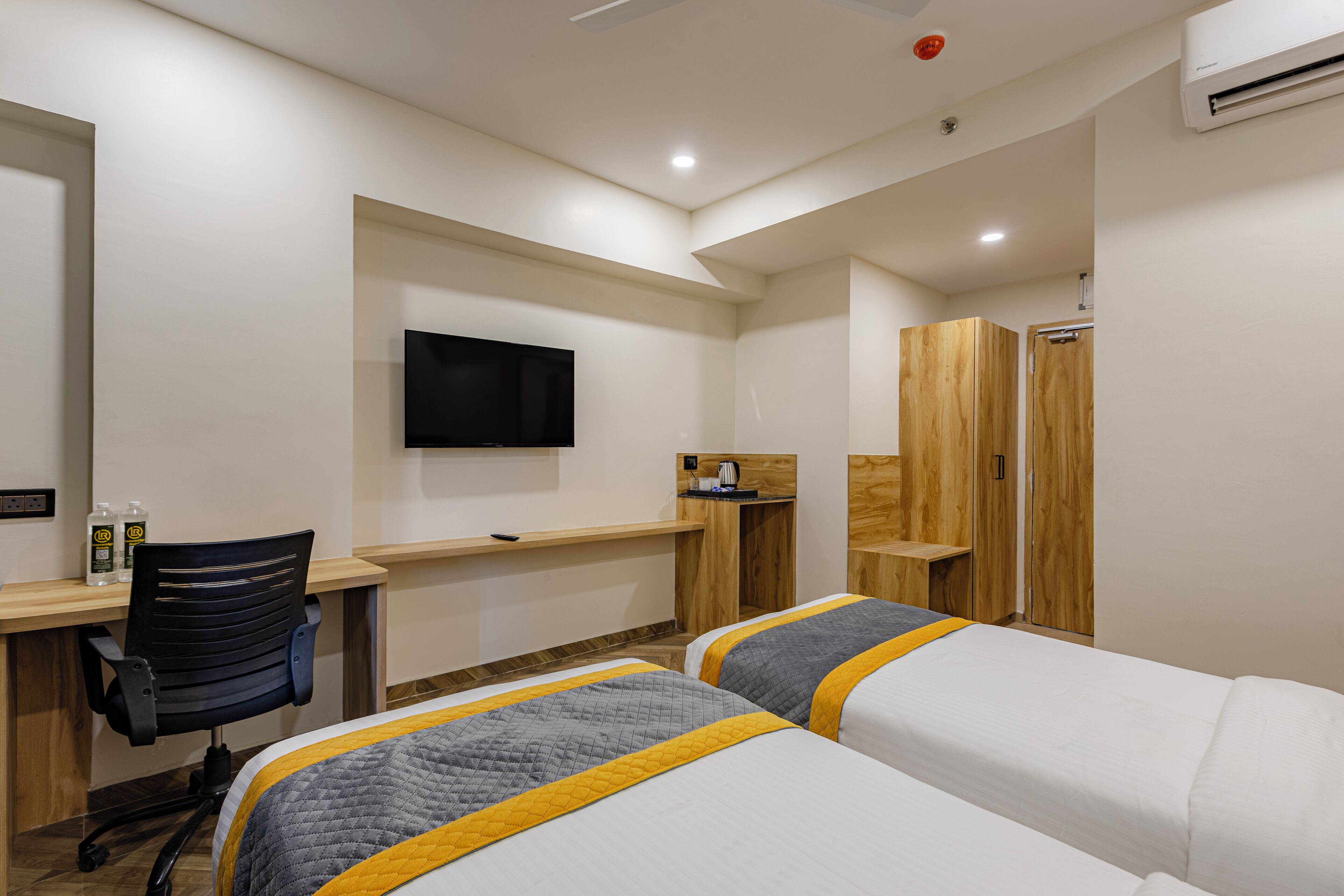 A hotel room with two beds, a desk, a chair, a TV, and a wardrobe.