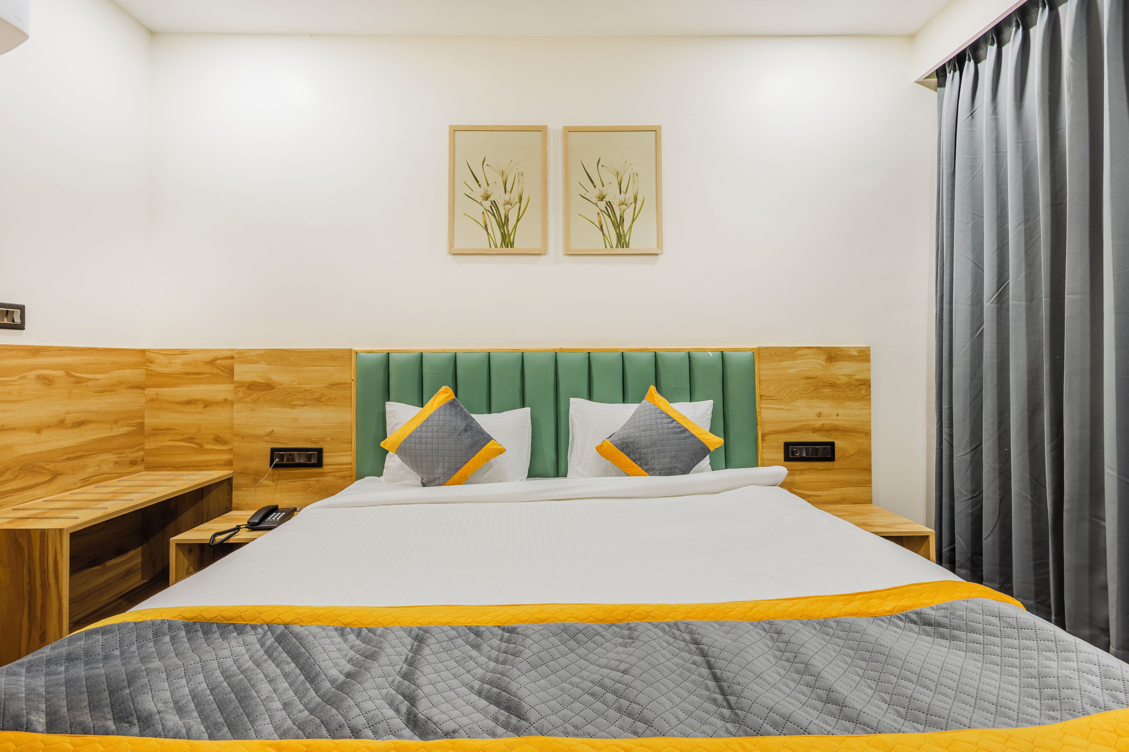 Ein Hotelzimmer mit einem hölzernen Kopfteil, einem Bett mit gesteppter Bettdecke, zwei Nachttischen mit Lampen und einem an der Wand befestigten Telefon.