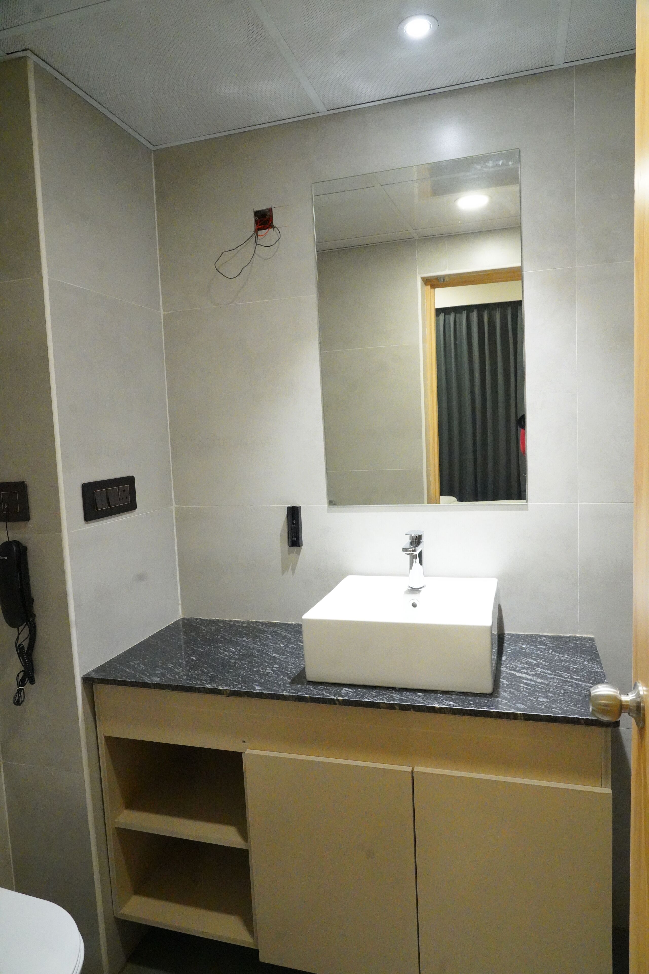 A bathroom with a white sink, a mirror, a telephone, and a door.