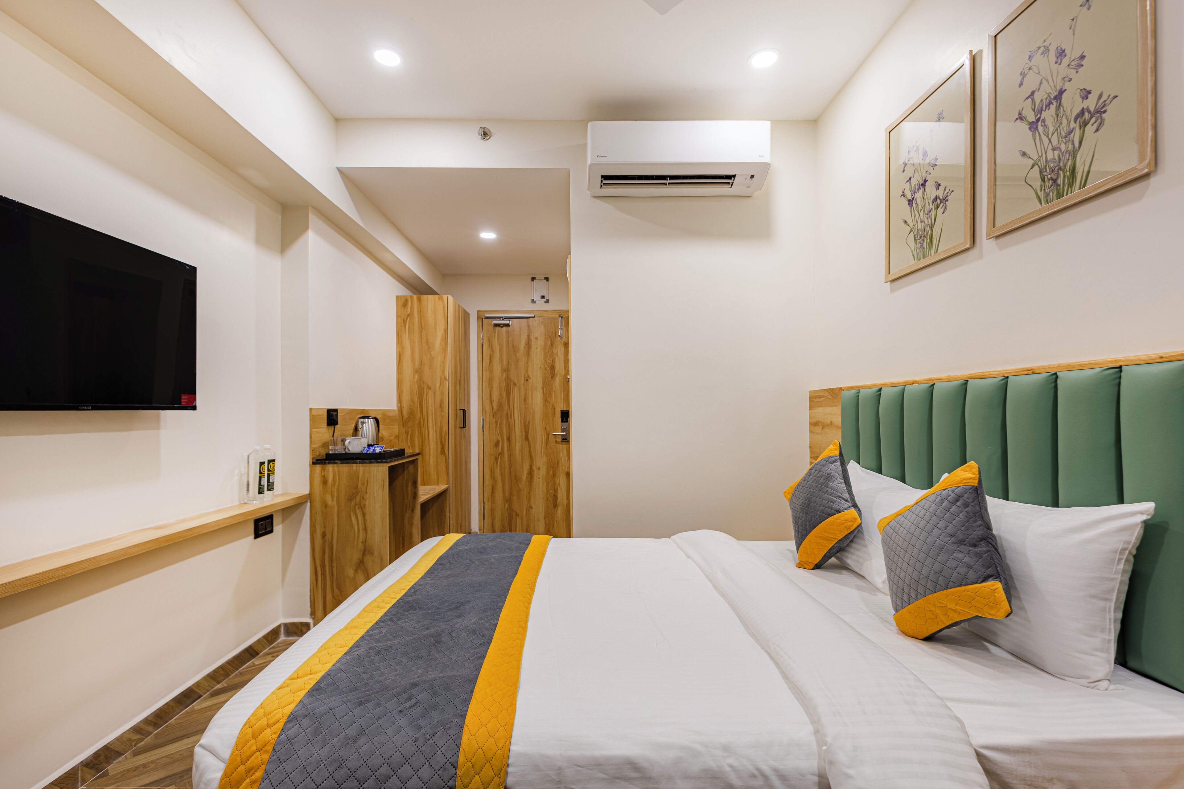 Ein Hotelzimmer mit Bett, Wandfernseher, Holzschrank und einer kleinen Küchenzeile.