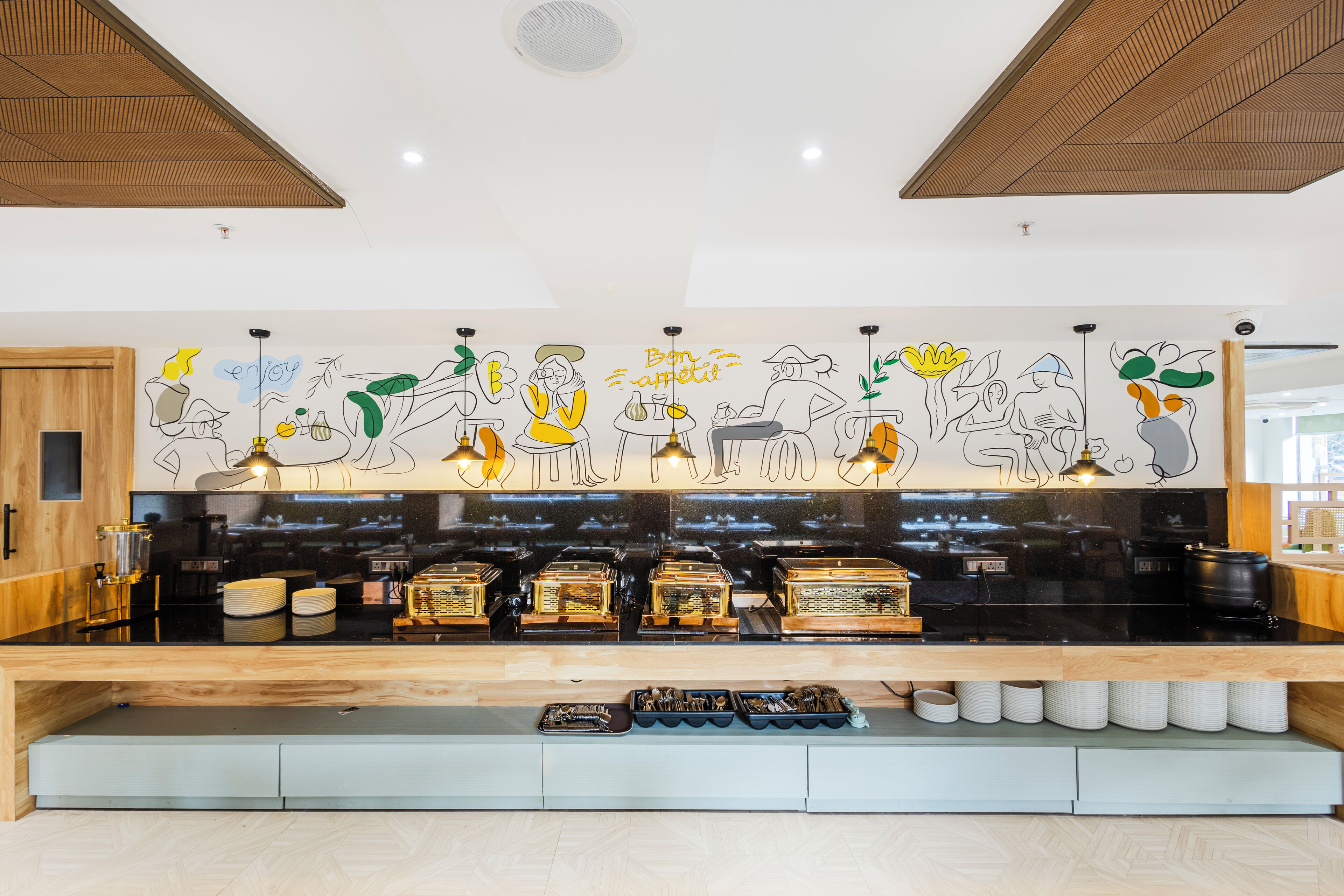 Une cuisine moderne avec un plan de travail en bois, des appareils électroménagers noirs et une fresque murale représentant des personnes à table.