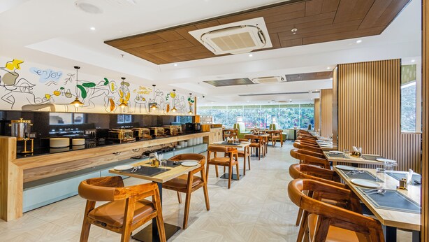 Un restaurante moderno con mobiliario de madera, una barra larga y vistas a zonas verdes a través de amplios ventanales.