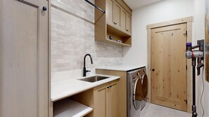 Una cocina compacta con encimera blanca, un lavamanos, armarios de madera y una lavadora.