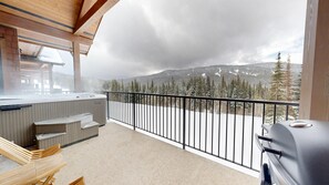 Un balcón con jacuzzi, zona de estar y vistas a montañas nevadas.