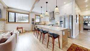 A modern kitchen with a central island, bar stools, and stainless steel appliances. - Switchback Creek Two #3 | 3 Peaks Rentals (Sun Peaks)